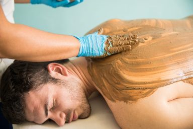 Handsome Latin young man getting a massage and a mud bath during his visit at a spa